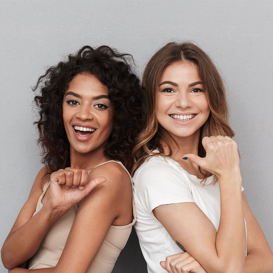 Zwei lachende Frauen zeigen auf sich gegenseitig